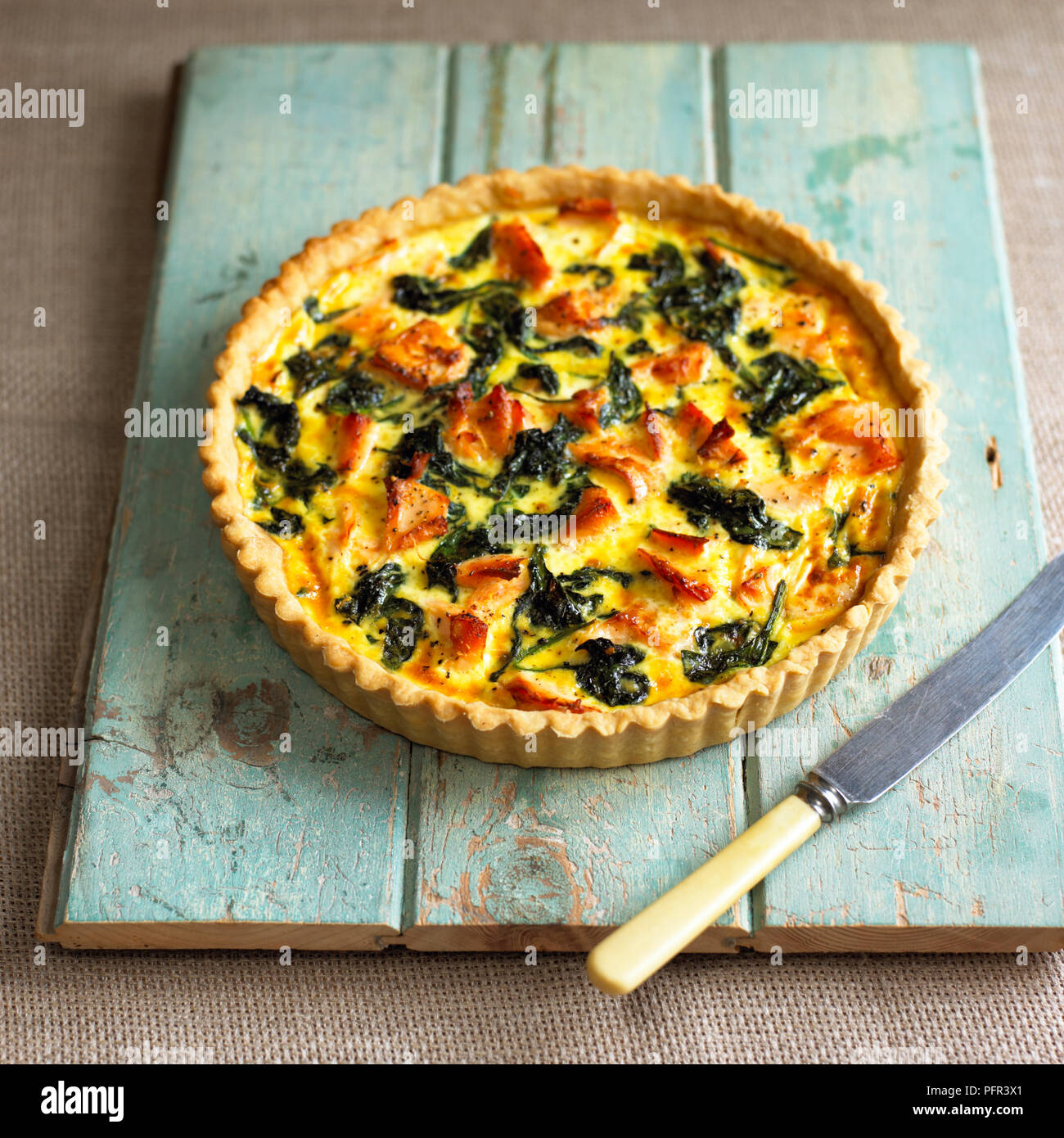 Salmon and spinach quiche on wooden board, knife nearby Stock Photo
