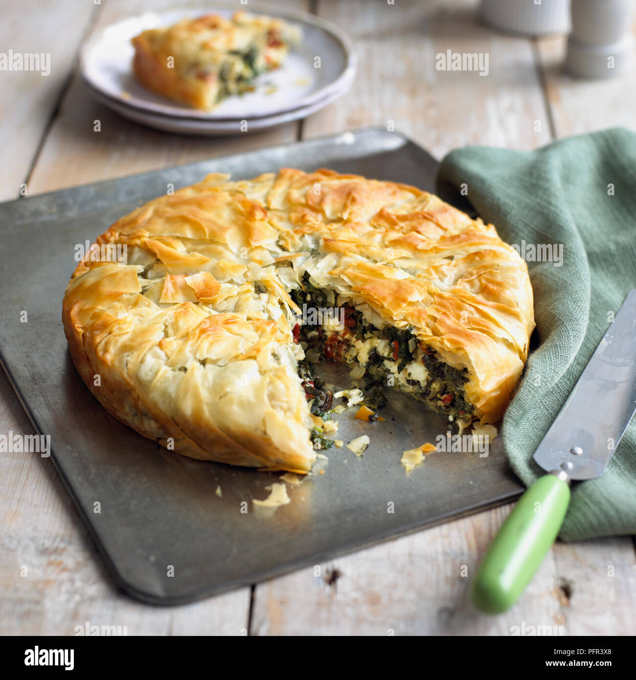 Herby feta filo pie with slice removed, spatula or palette knife nearby Stock Photo