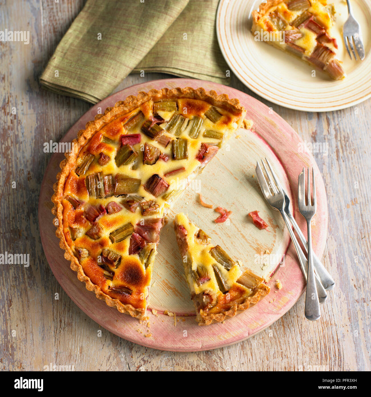 Rhubarb and custard tart with a slice cut away, dessert forks, on wooden plate Stock Photo