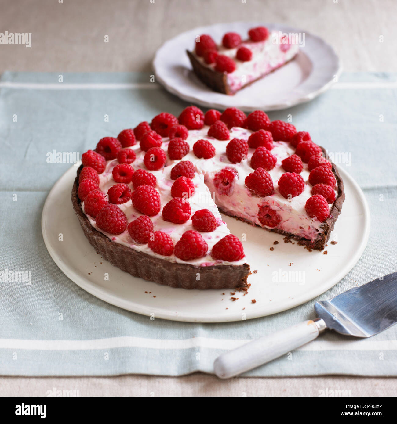 Double chocolate raspberry tart with single slice cut away, seen on plate in background Stock Photo