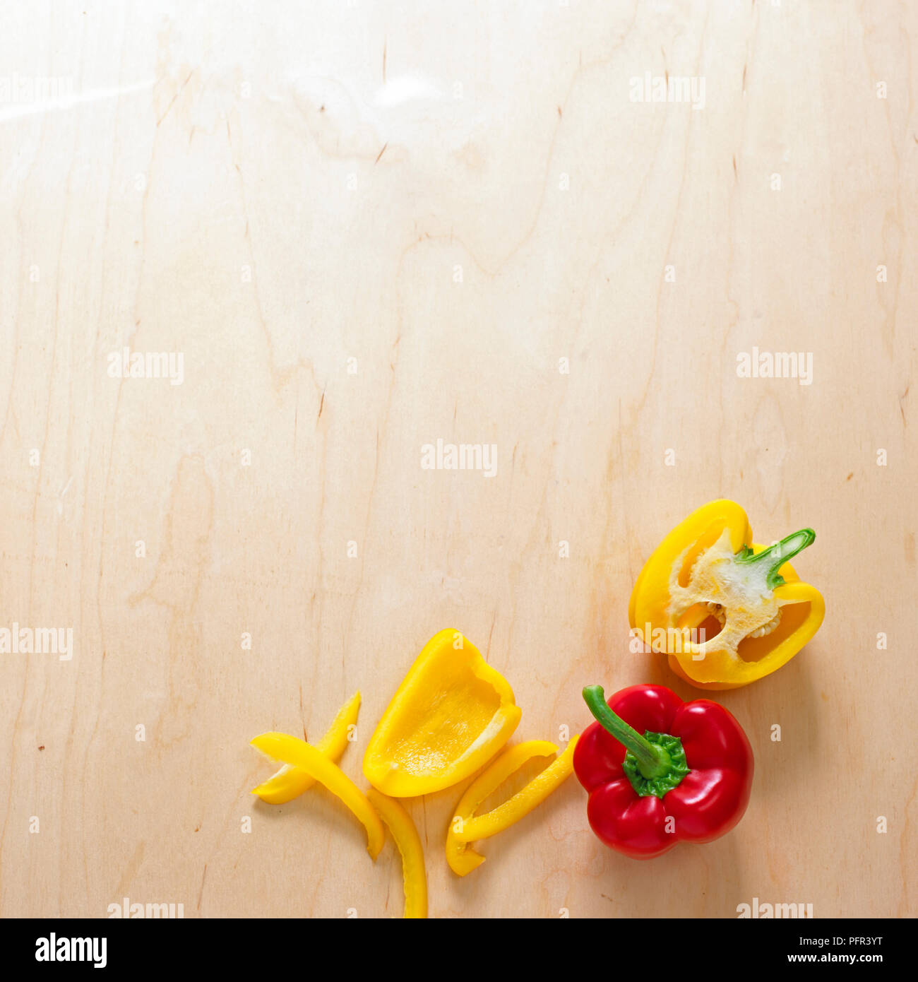 Whole, halved, cored and sliced bell peppers on wooden surface Stock Photo