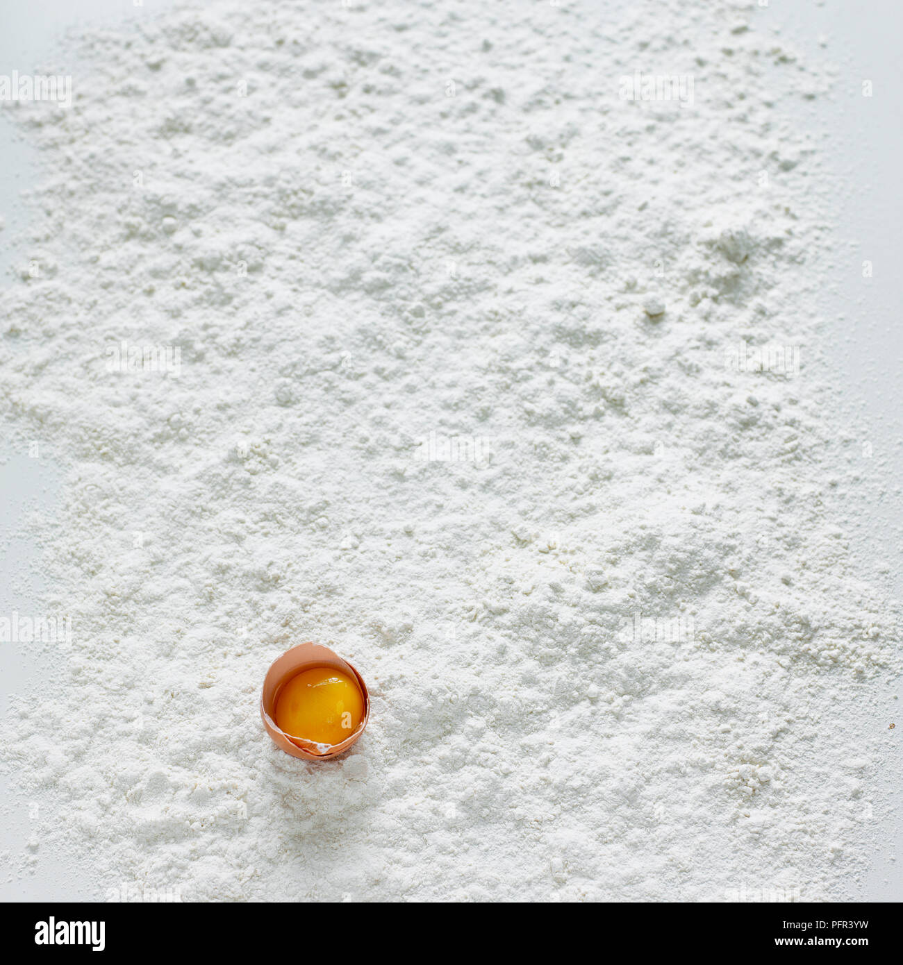 Egg yolk, separated from egg white, in eggshell on flour-covered surface Stock Photo