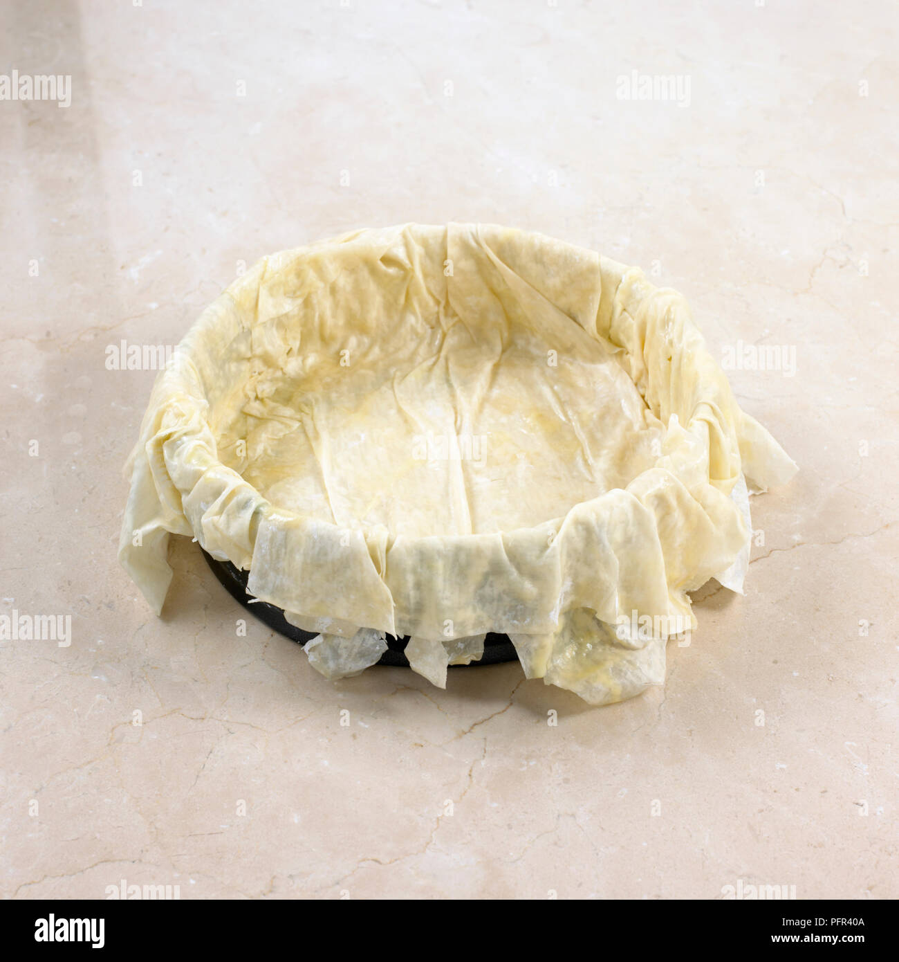Making filo pie, five sheets of filo pastry layered in springform tin