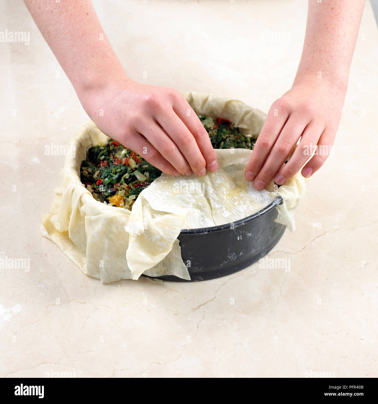 Making herby feta filo pie, adding half the filling, then feta, then filling, putting overhanging pastry over the top Stock Photo