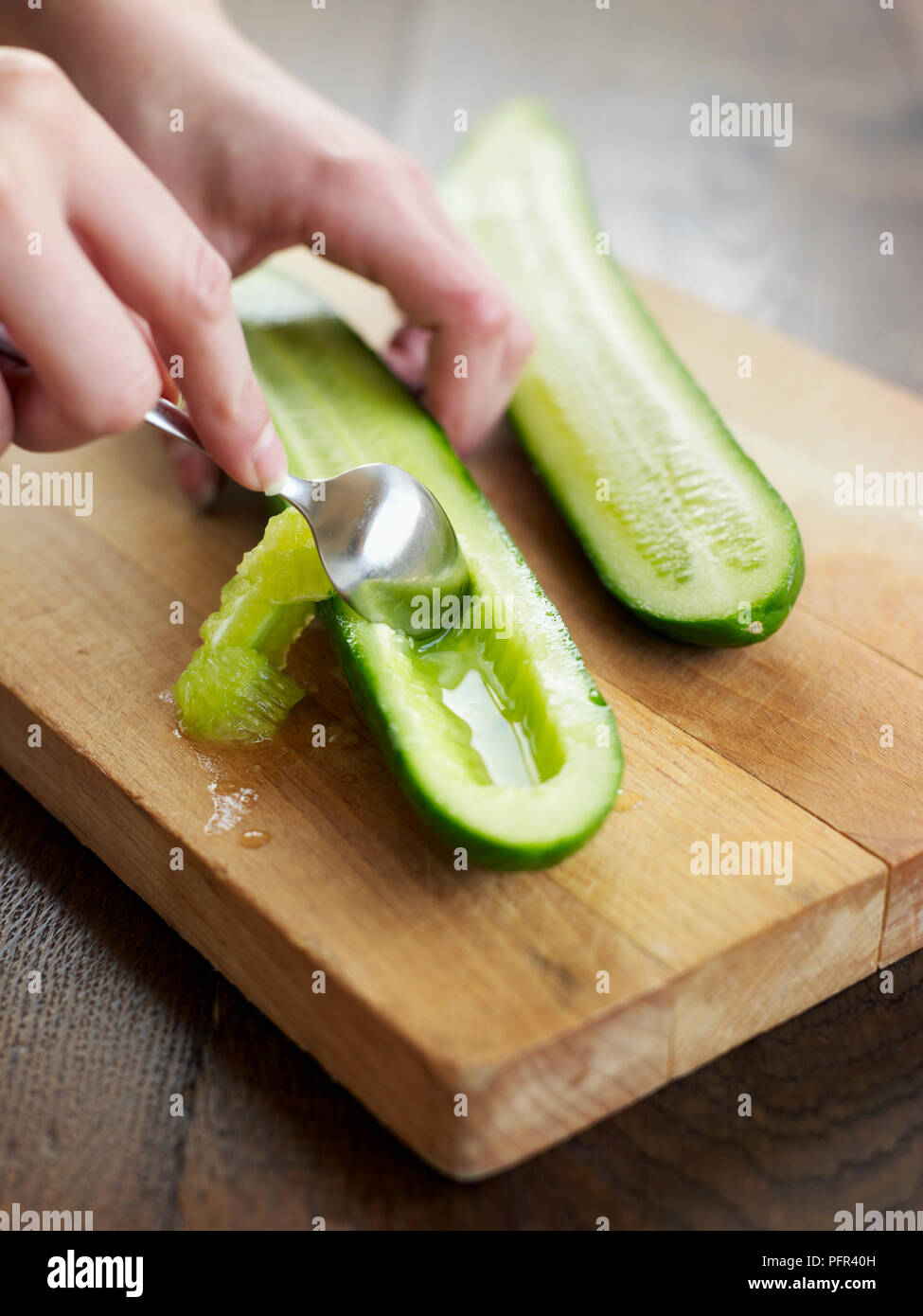 Cucumbers cut in half lengthways and having seeds removed with spoon Stock Photo