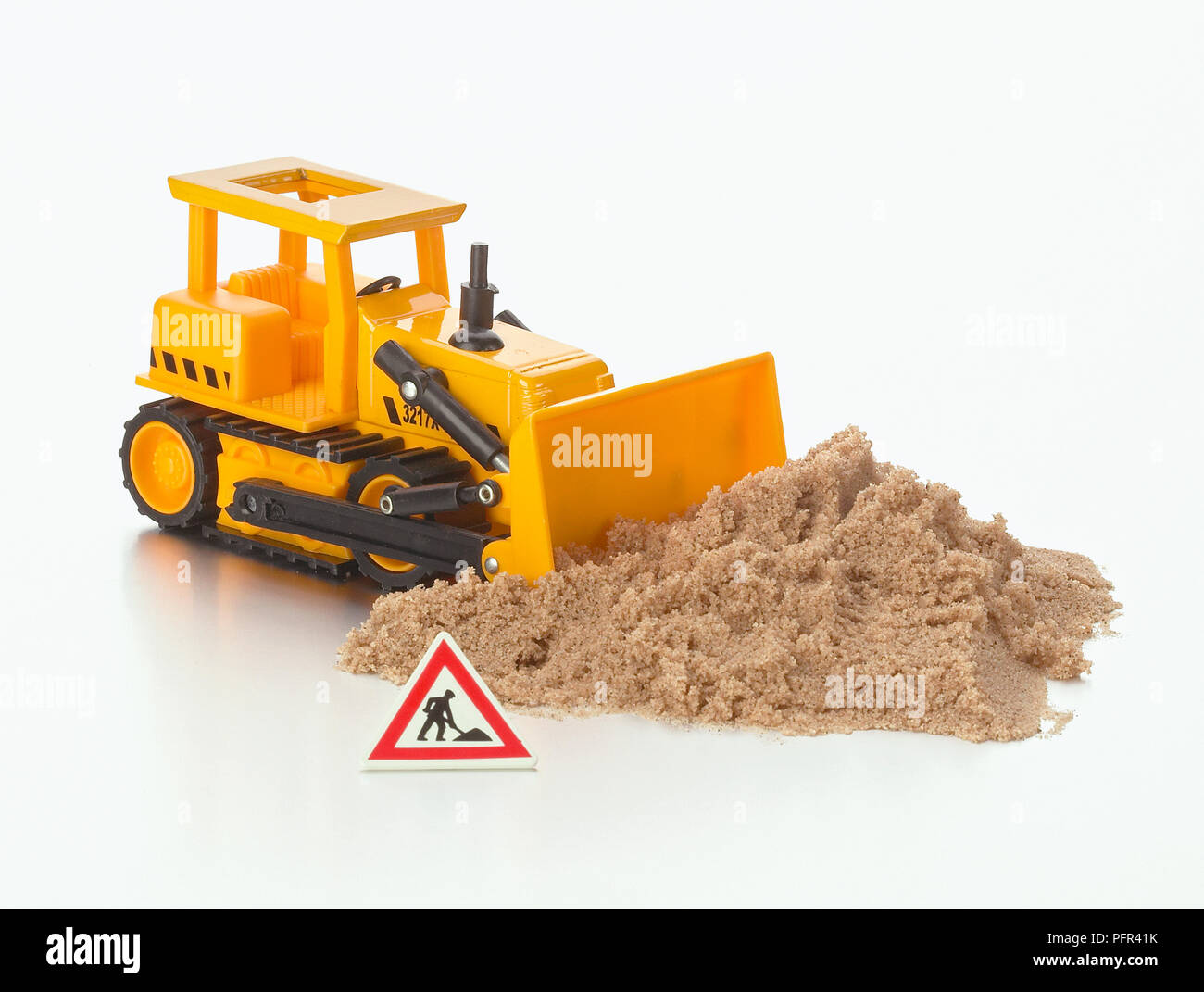 Toy bulldozer, pile of sand, and construction site warning sign Stock Photo