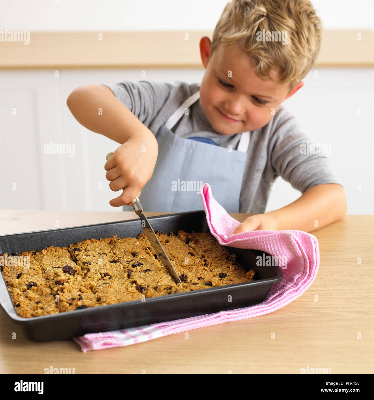 Boy cutting muesli bars in a tray, 4 years Stock Photo