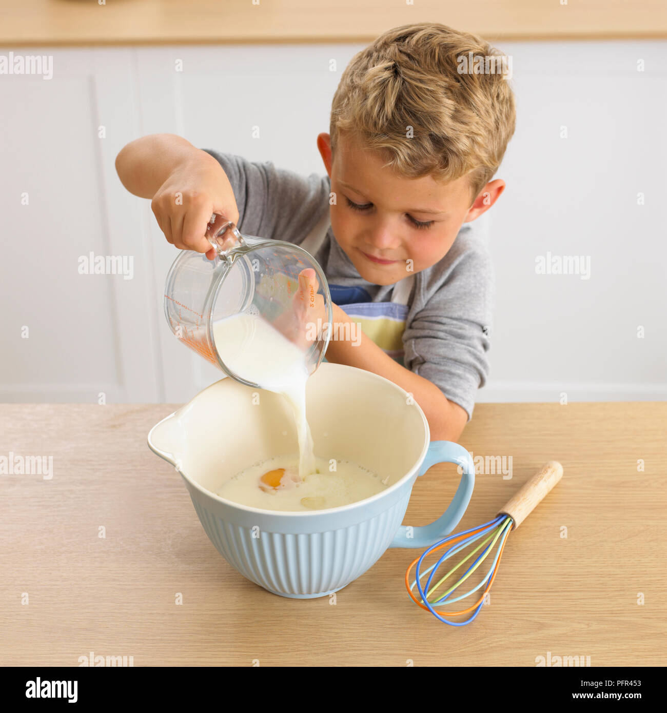 Boy pouring milk into jug of eggs, 6 years Stock Photo