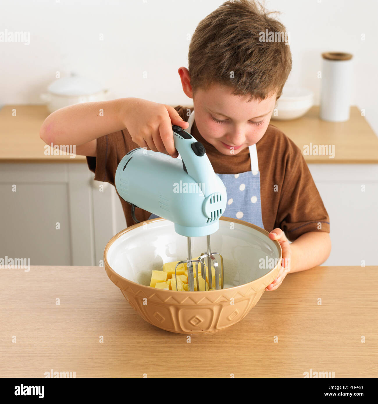 Boy mixing bowl of butter and sugar using electric mixer, making a cake