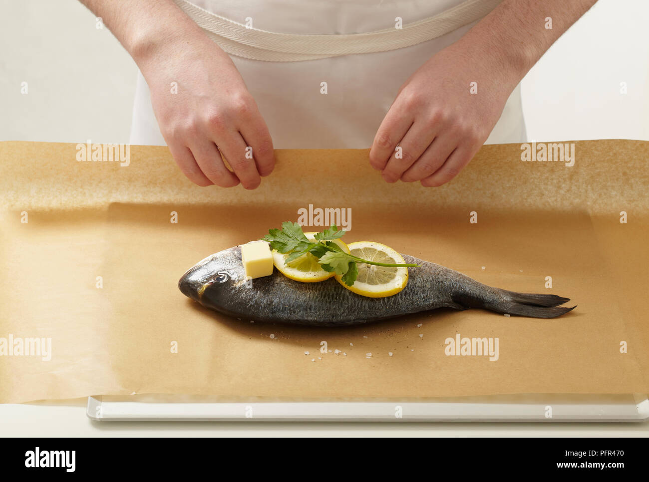 Wrapping whole sea bream in baking paper, with lemons, herb, and butter Stock Photo