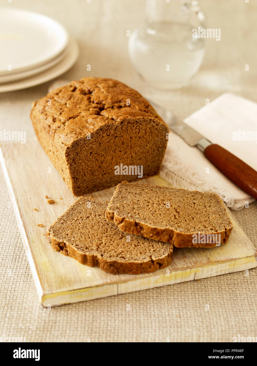 Gluten free basic brown loaf on chopping board with two slices and bread knife Stock Photo