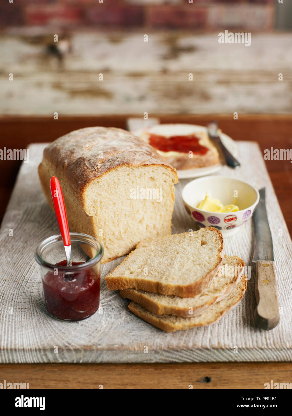 Sliced loaf of bread on wooden board with jam and butter Stock Photo