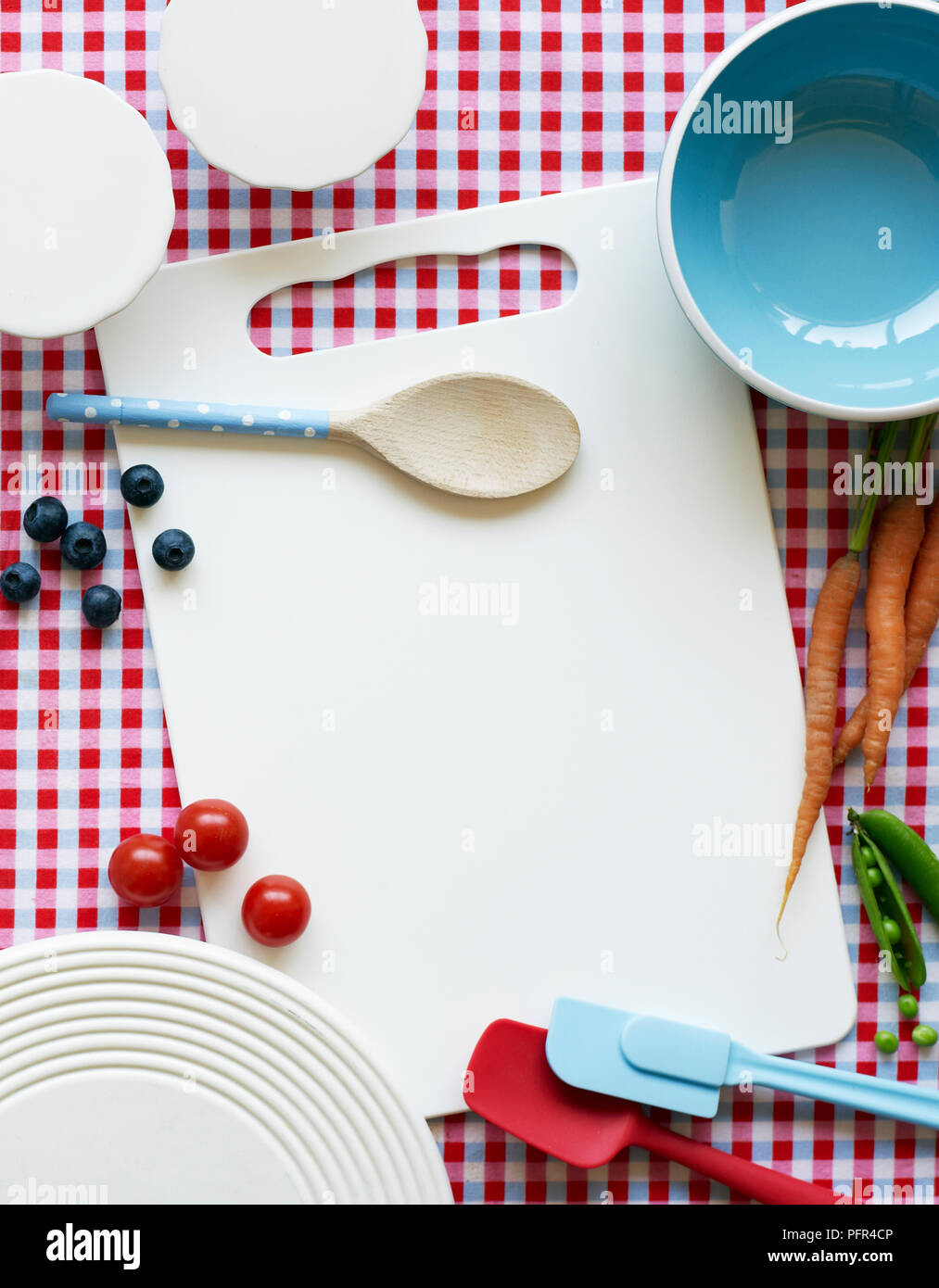 Various kitchen tools, including wooden spoon, chopping board, and spatulas, on red and white checked surface Stock Photo