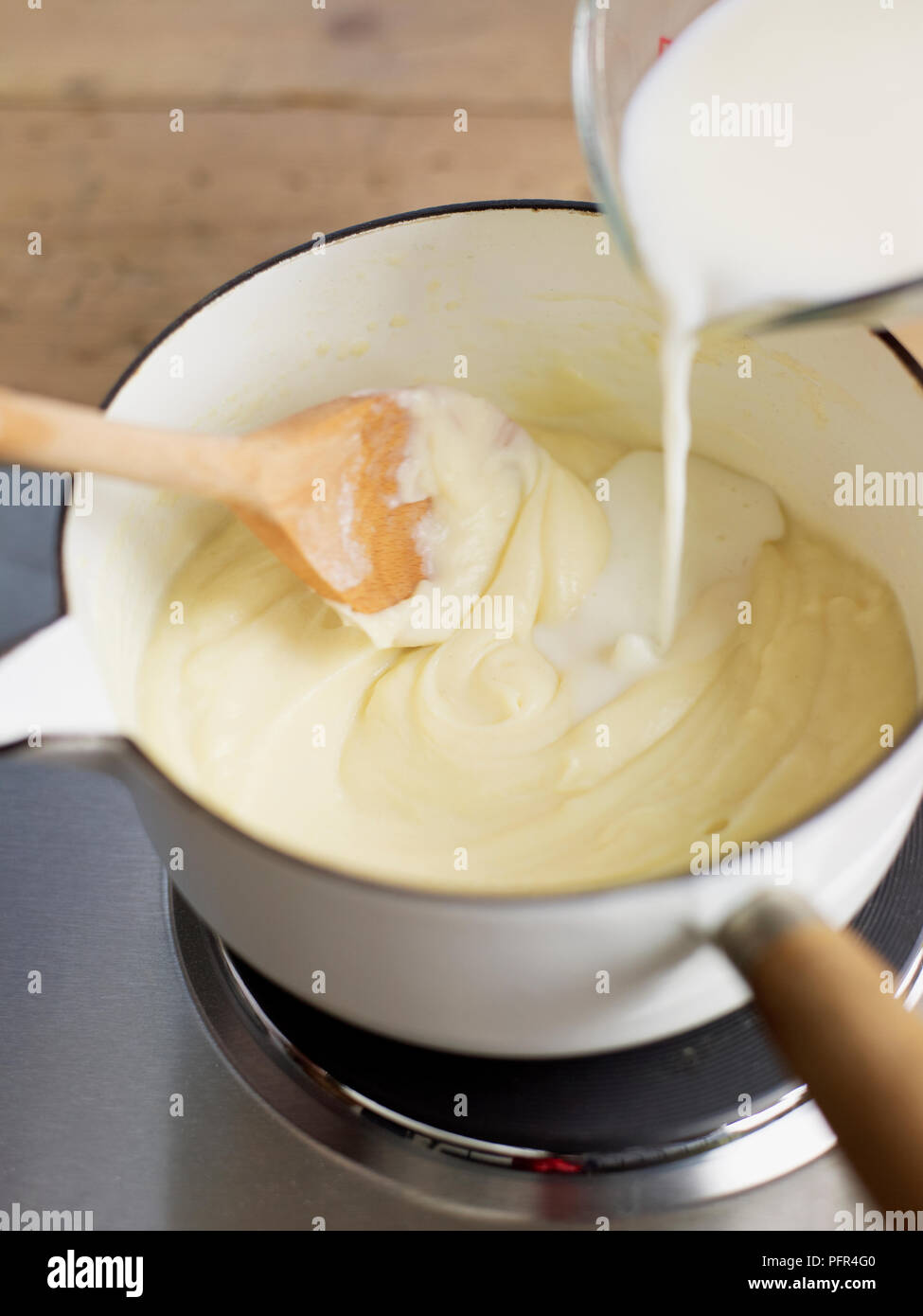 Pouring milk into roux while stirring (cooking bechamel sauce Stock