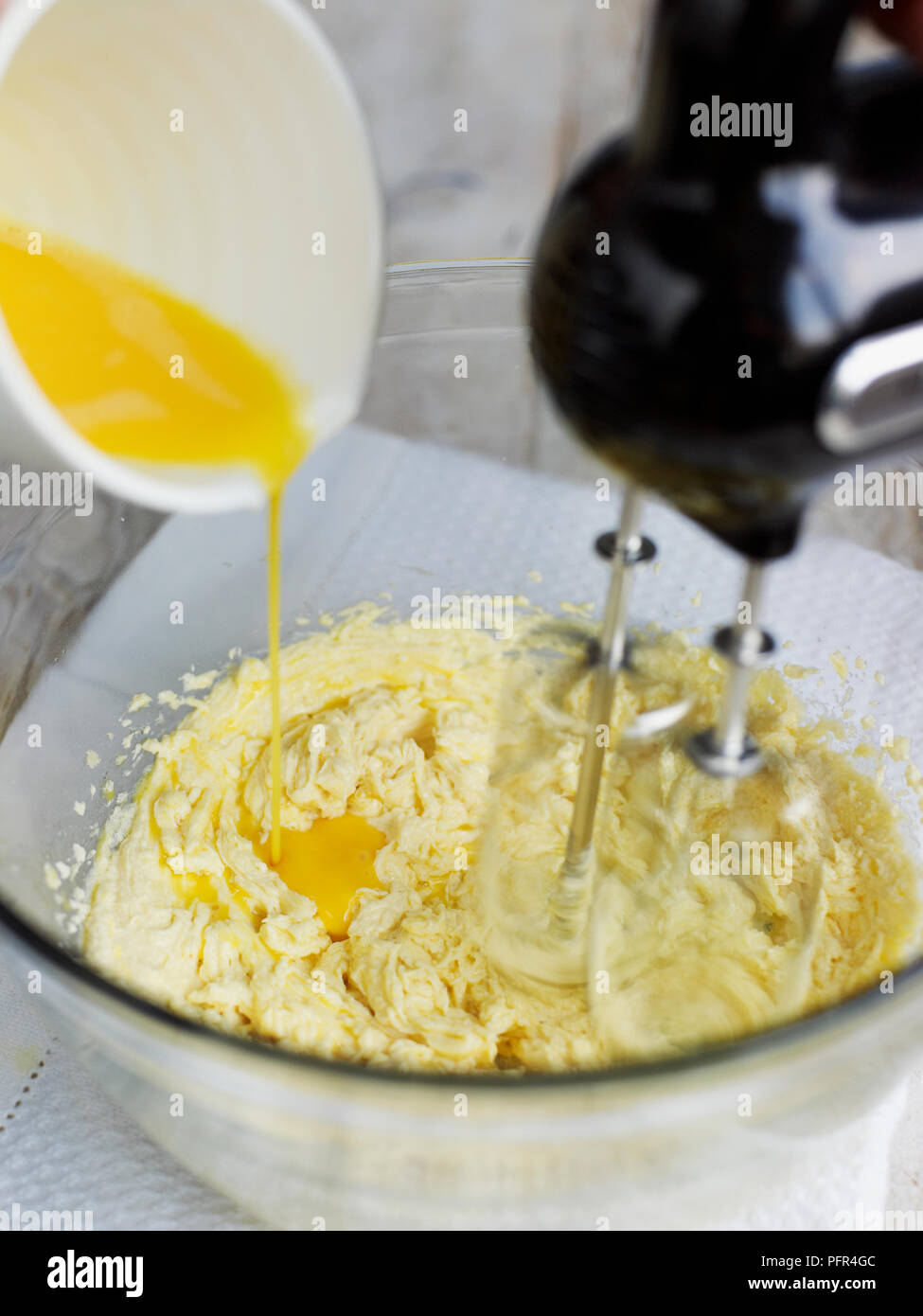 Adding eggs to Victoria sponge cake mixture in mixing bowl, using electric mixer Stock Photo