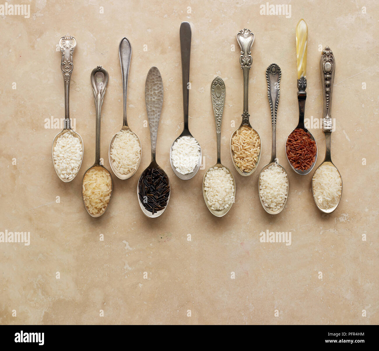 Spoons containing different types of rice, risotto rice, long-grain rice, basmati rice, wild rice, sticky rice, pudding rice, brown rice, sushi rice, red rice (camargue rice), jasmine rice Stock Photo