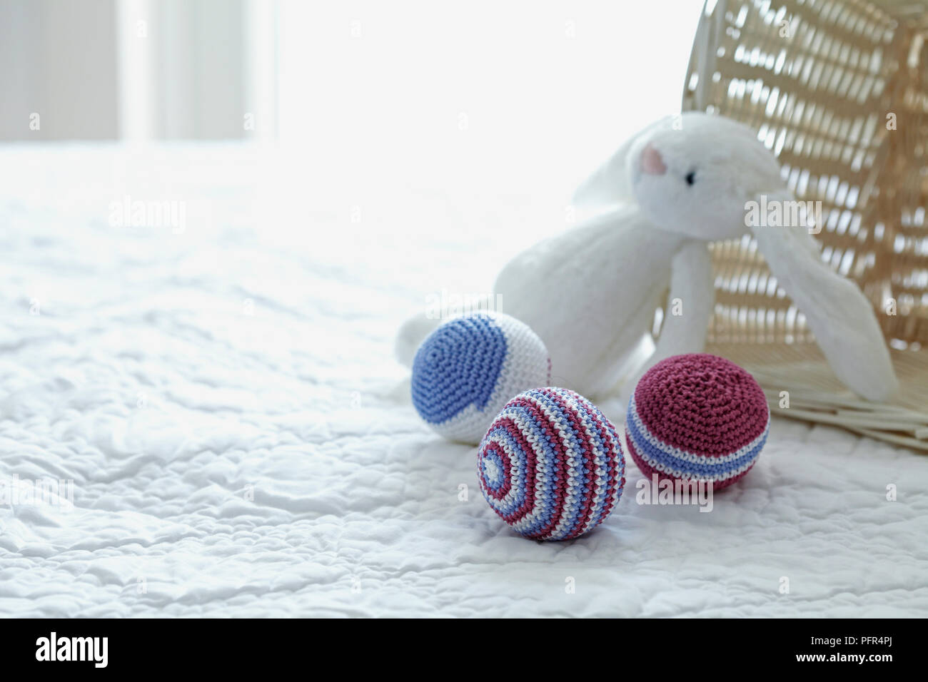 Crocheted toy balls and stuffed toy rabbit on a bed Stock Photo