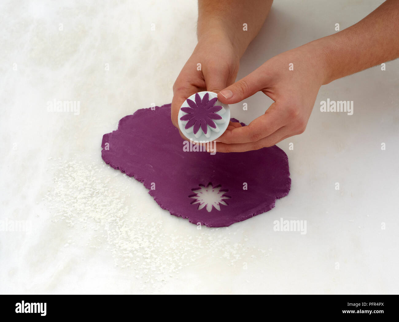 Cutting flower shape from purple fondant using plunger cutter, making cake decorations Stock Photo