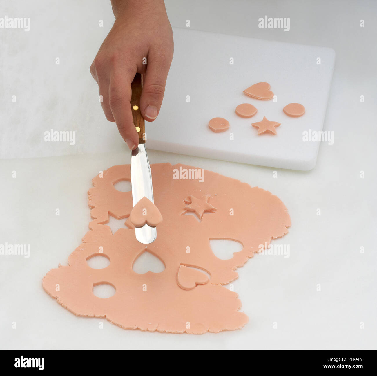 Cutting decorative shapes out of pink fondant, making cake decorations Stock Photo