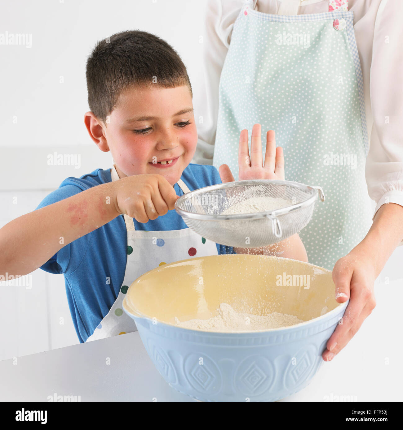 Boy sifting flour into a mixing bowl, 7 years Stock Photo