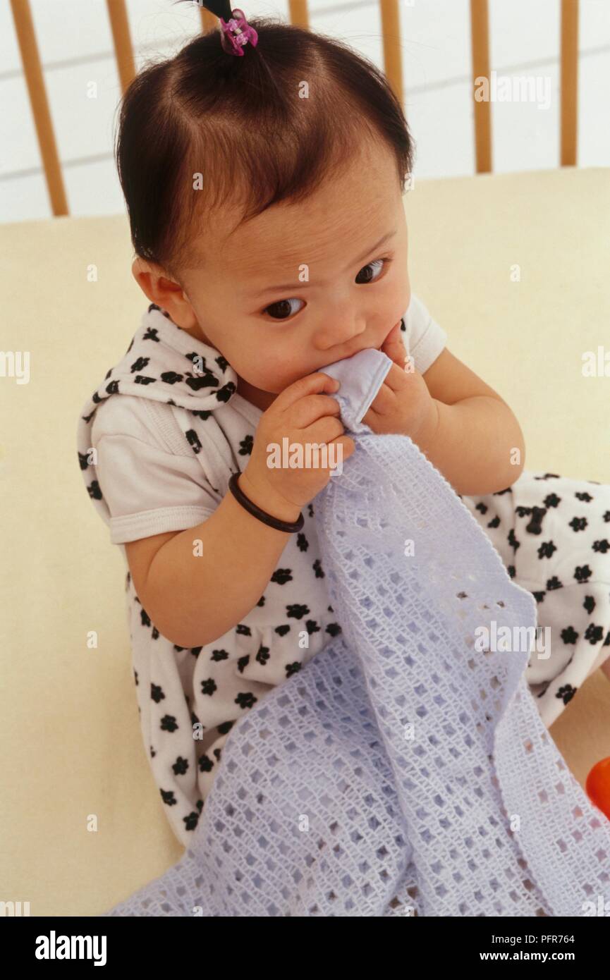 Baby girl sat chewing her blanket Stock Photo