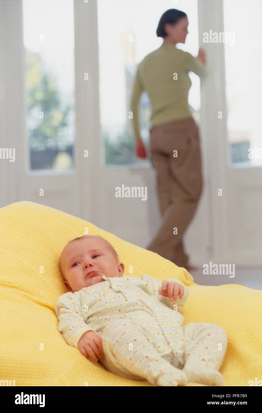 Baby lying in blanket, woman standing by window in the background Stock Photo