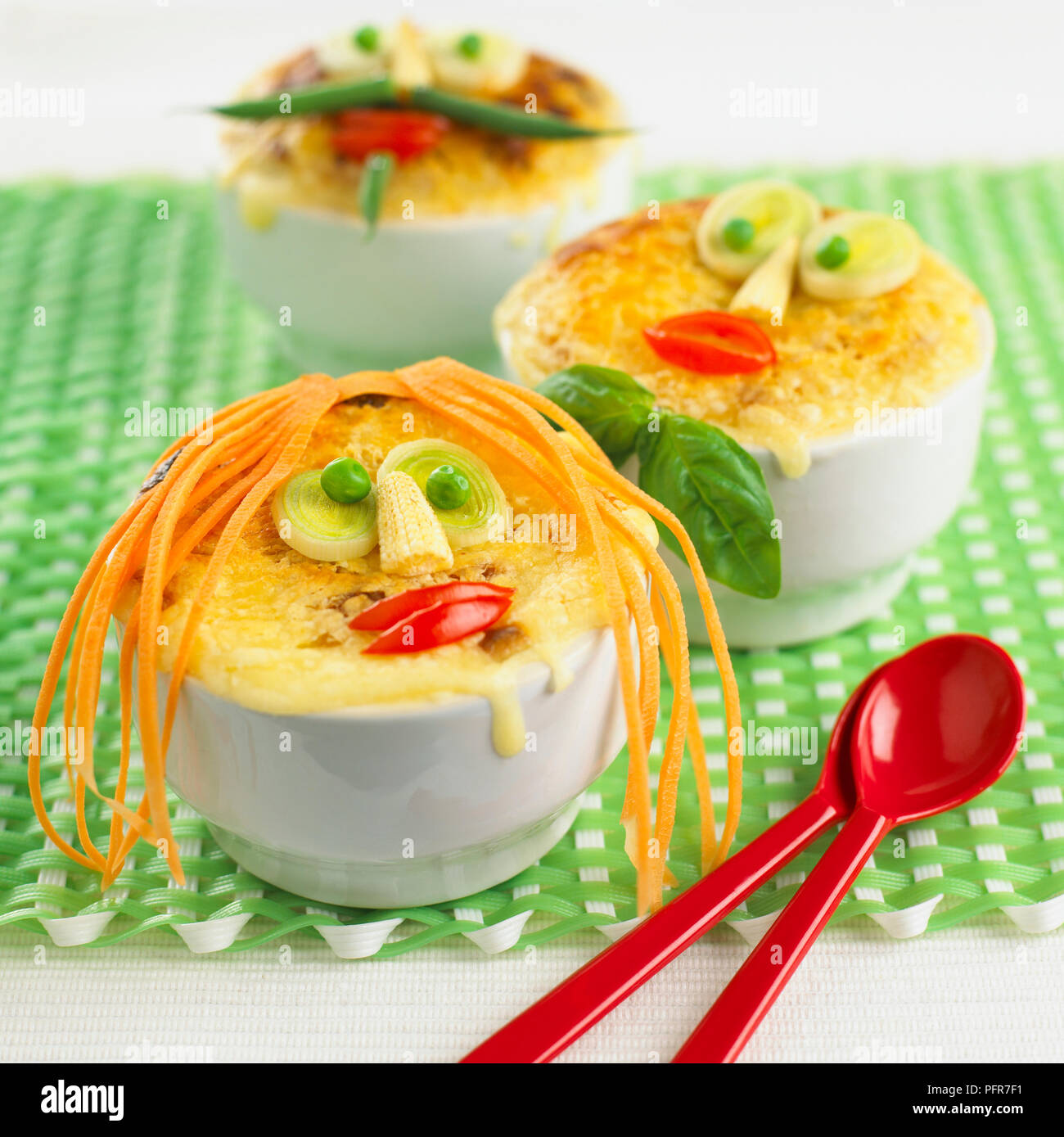 Child's potato and leek pies decorated with funny faces in white bowls, on place mat Stock Photo