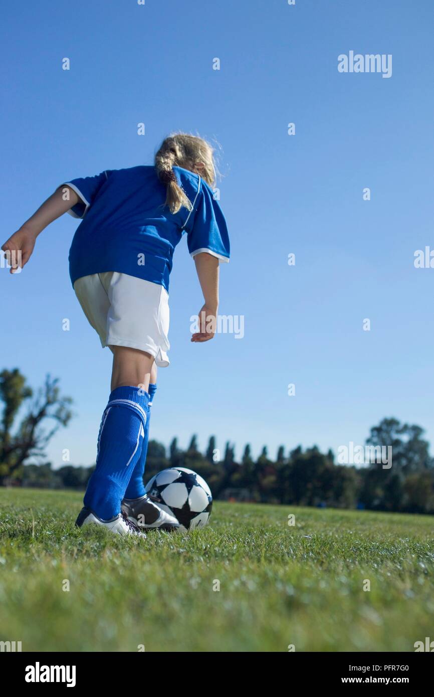 Girl in football gear standing pushing ball forward with her foot