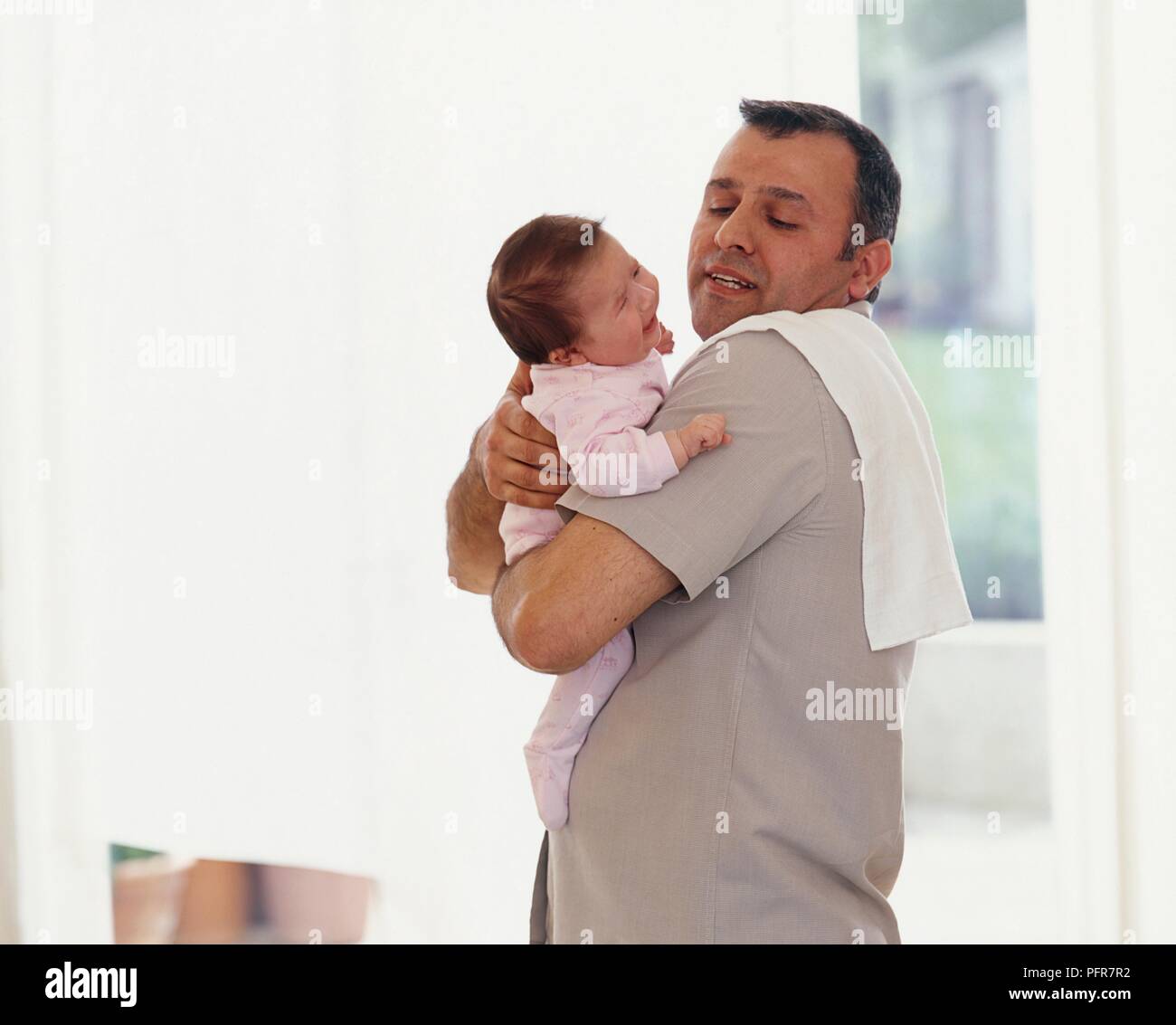 Man holding baby girl securely in his arms, cloth on his shoulder Stock Photo