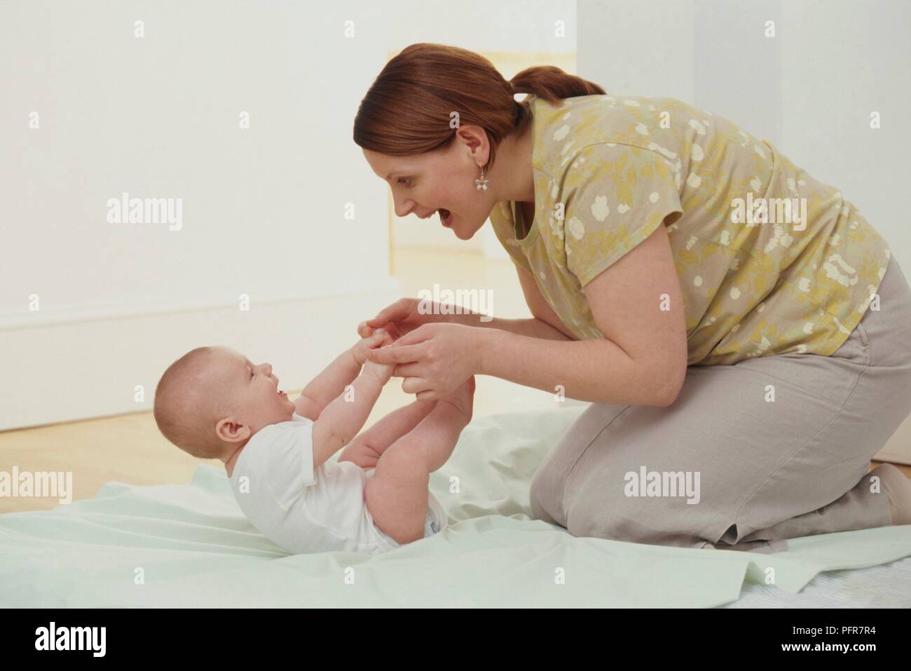 Woman kneeling on mat holding baby boy's hands and pulling him up from blanket Stock Photo Alamy