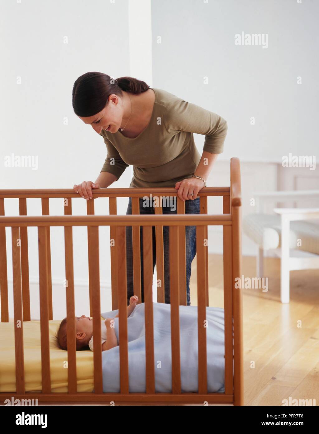 Woman looking down at baby lying in cot Stock Photo