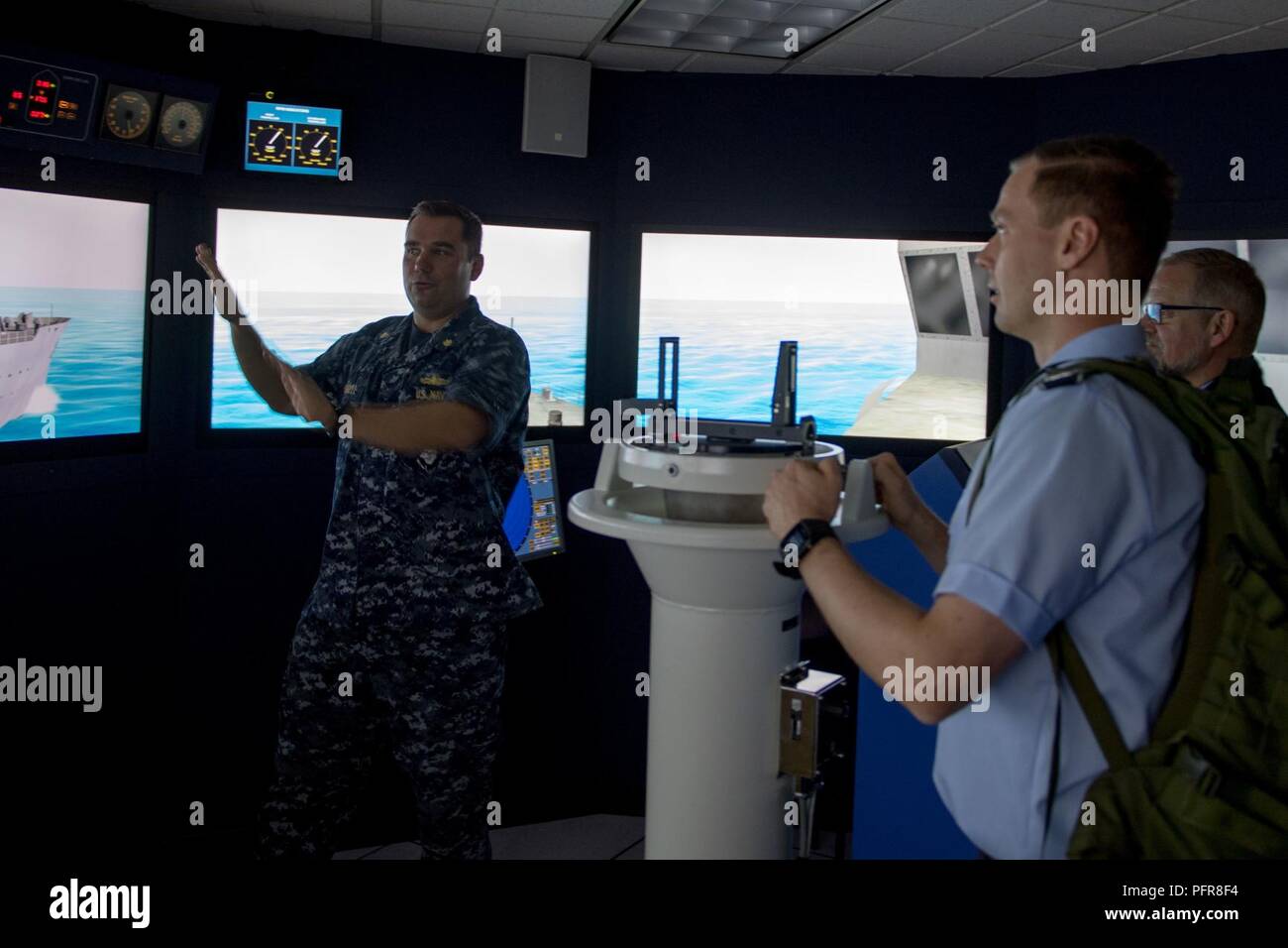 Everett, Wash. (May 21, 2018) Lt. Cmdr. Matt Farrell, executive officer of Afloat Training Group Pacific Northwest, explains the duties of a conning officer to German Army officer, Maj. Joachim Ruthe, in the navigation, seamanship and ship handling trainer in Naval Station Everett (NSE). Ruthe and his fellow officers are enrolled in the International General/Admiral Staff Officer Course and are touring NSE. Stock Photo
