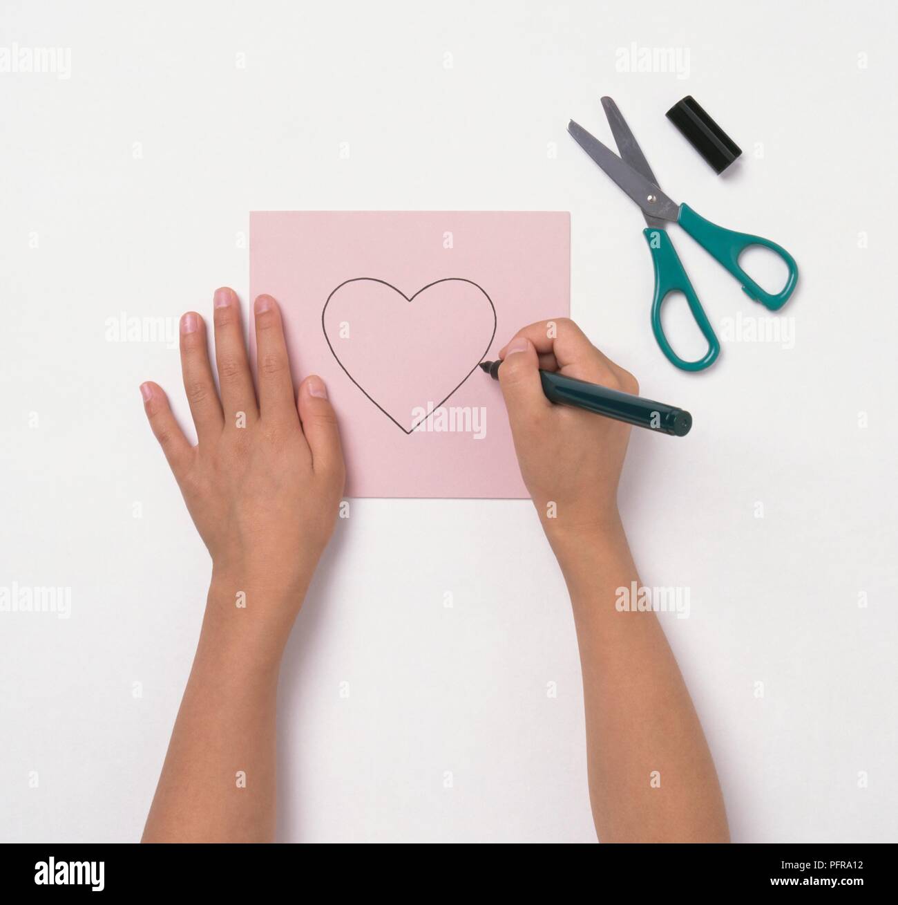 Girl using felt tip pen to draw heart shape on pink paper Stock Photo