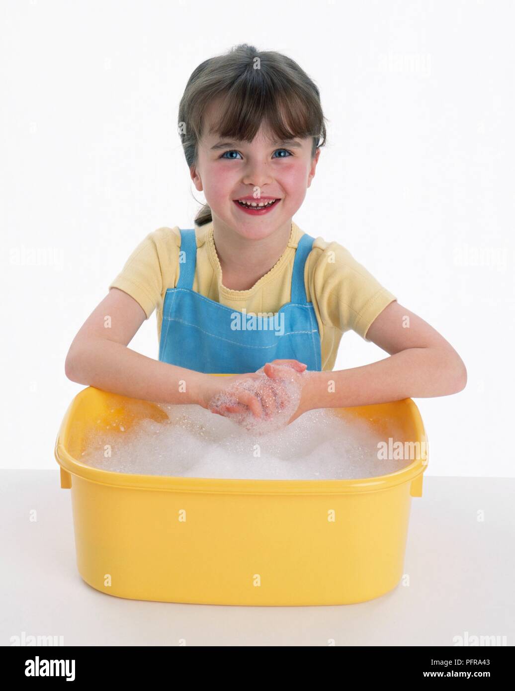 Five year old girl washing her hands in yellow plastic washing tub