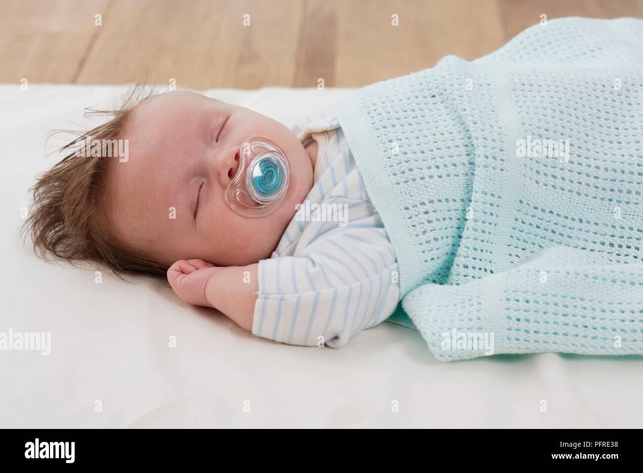 Baby boy lying down with dummy in his mouth and covered with baby blanket Stock Photo