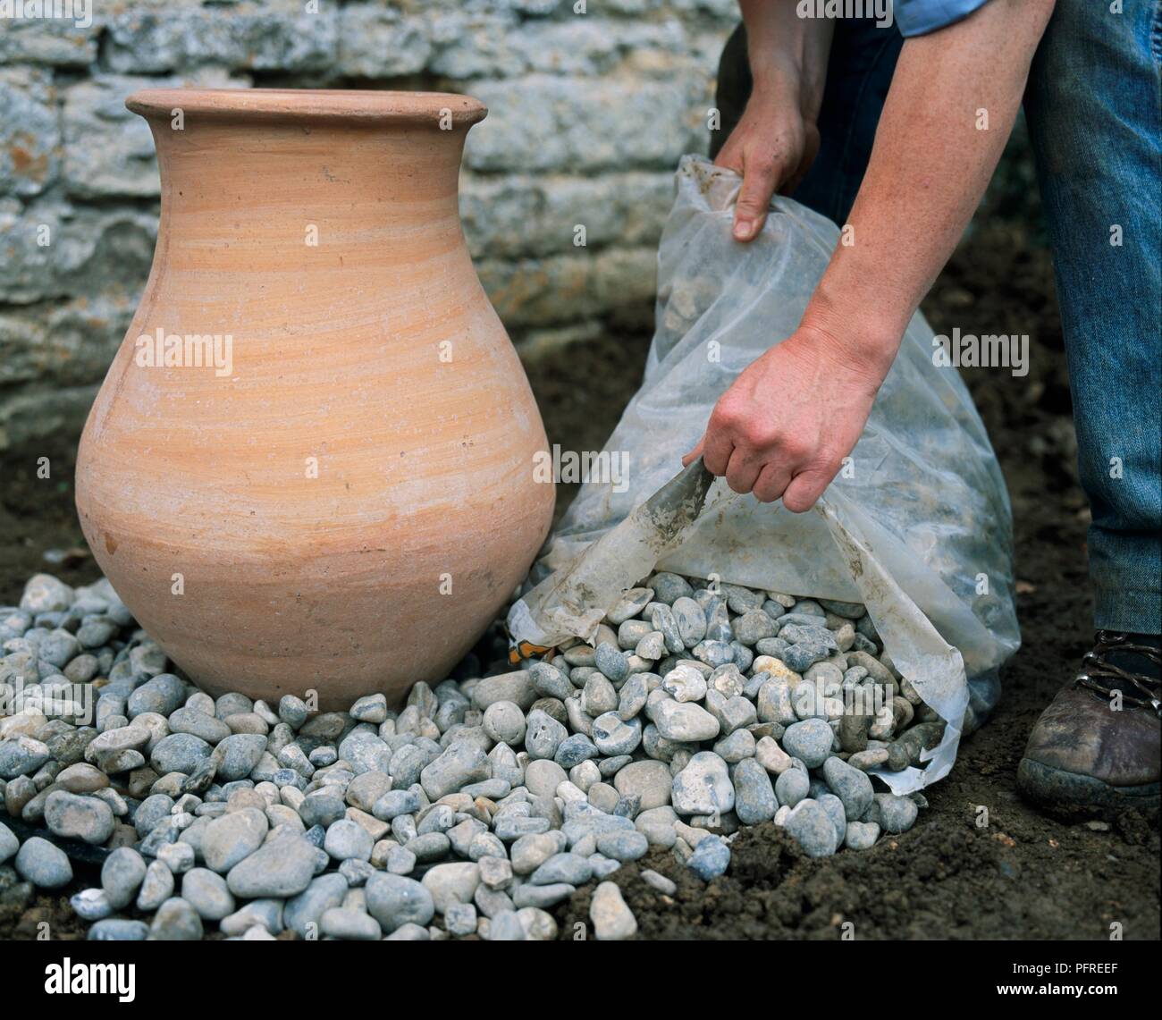Arranging pebbles around terracotta urn (making a water feature), close