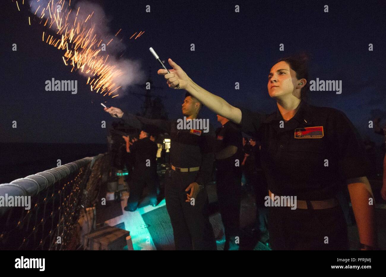 PHILIPPINE SEA (May 28, 2018) Ensign Lauren Kearney, the strike officer aboard the Arleigh Burke-class guided-missile destroyer USS Benfold (DDG 65), lights off pencil flares from the ship’s fantail after a promotion ceremony on Memorial Day. Benfold frocked 38 Sailors to the next paygrade and promoted 6 officers to lieutenant junior grade on Memorial Day while underway. Benfold is forward-deployed to the U.S. 7th fleet area of operations in support of security and stability in the Indo-Pacific region. Stock Photo