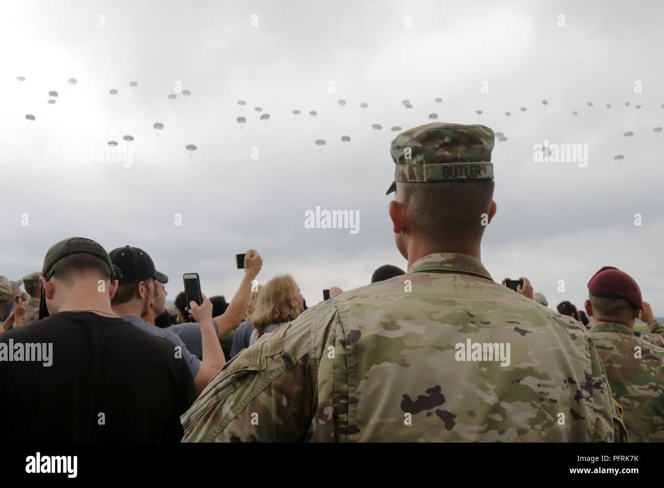 Future Soldiers and U.S. Army recruiter Staff Sgt. Adam Butler, assigned to the Raleigh Recruiting Battalion, watch paratroopers descend from sky during the 82nd Airborne Division’s Airborne Review at Sicily Drop Zone on Fort Bragg, North Carolina, May 24, 2018. Approximately 350 future Soldiers and recruiters from Raleigh Recruiting Battalion attended the Airborne Review and toured Fort Bragg during All American Week. Stock Photo