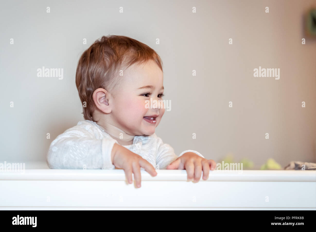 Portrait of a cute little baby boy at home standing in the crib, sweet child having fun in his bedroom, happy healthy childhood Stock Photo