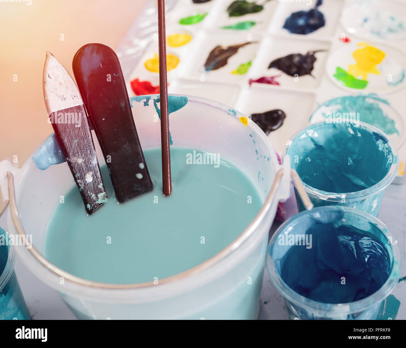 Artist paintbrushes in white bucket of water, acrylic colour in plastic