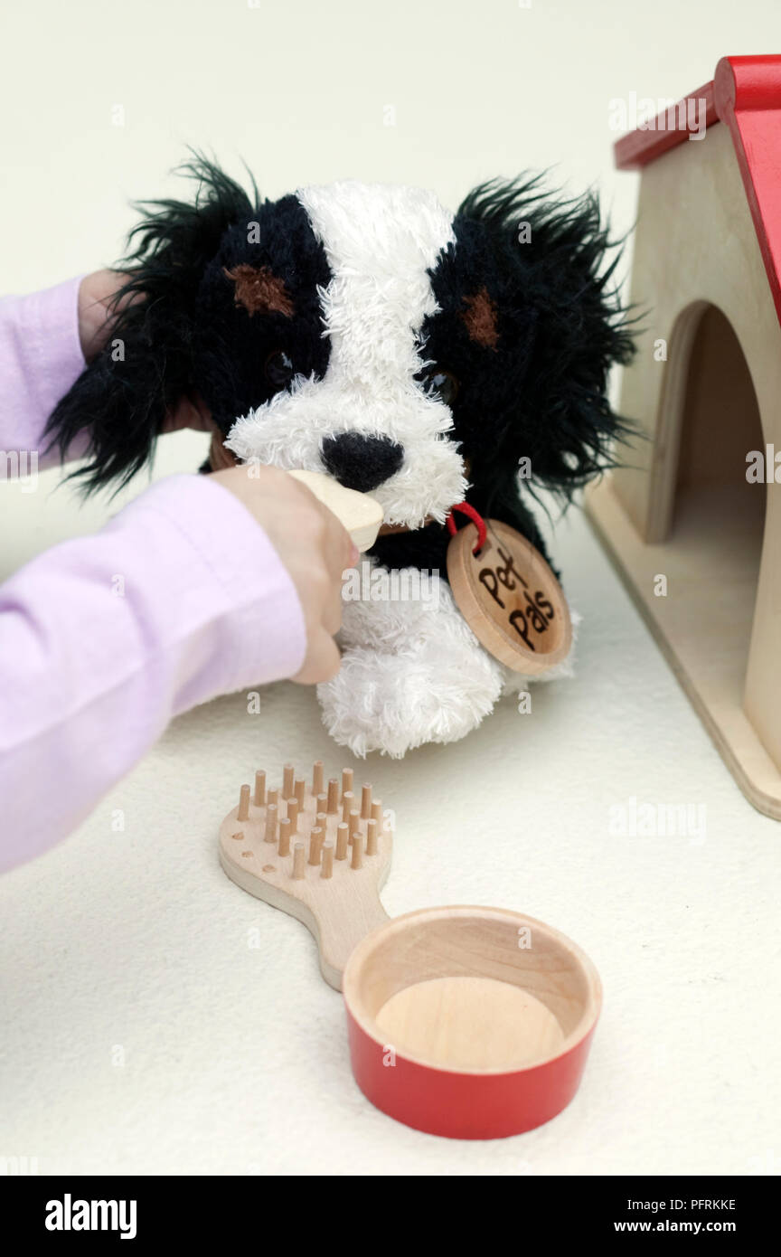 Girl playing with black and white toy dog next to toy kennel, close-up Stock Photo