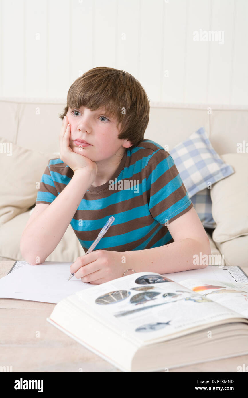 Boy sitting at table with pen in his hands, chin resting on the other