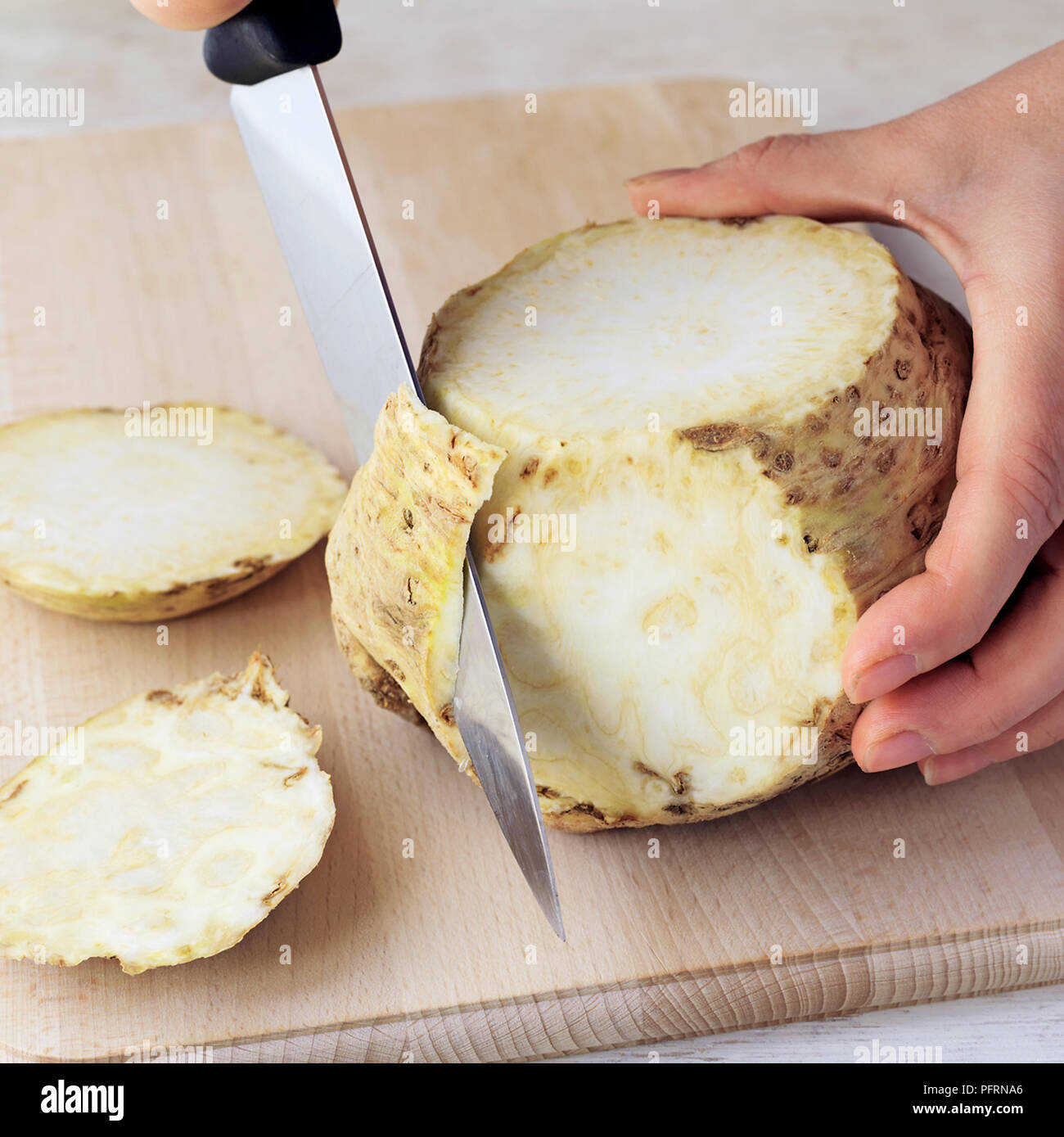 Person using knife to cut rough outer surface from celeriac on wooden chopping board on kitchen worktop, close-up Stock Photo
