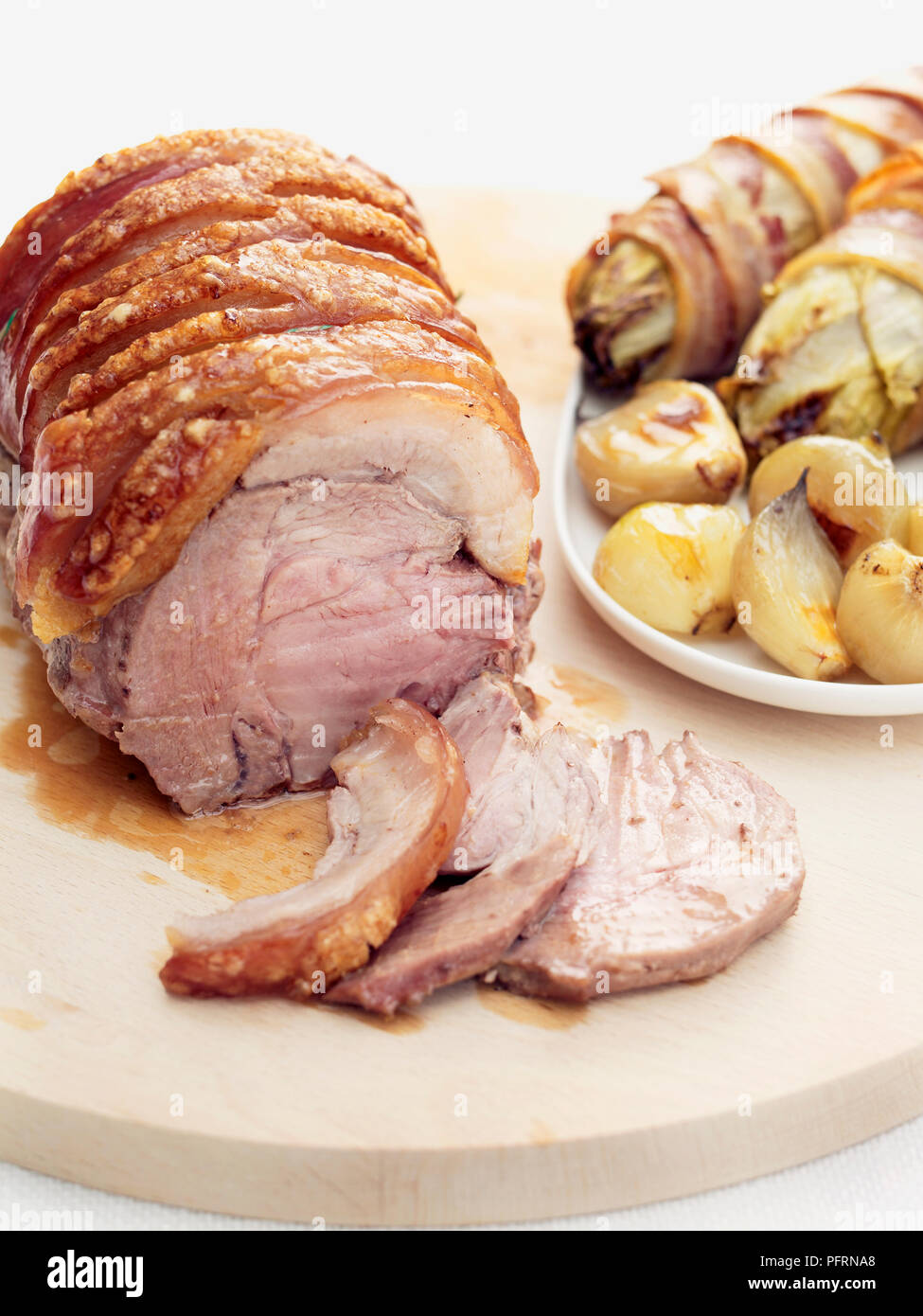 Roast pork wrapped in bacon, with chicory and onions on wooden chopping board and white plate Stock Photo