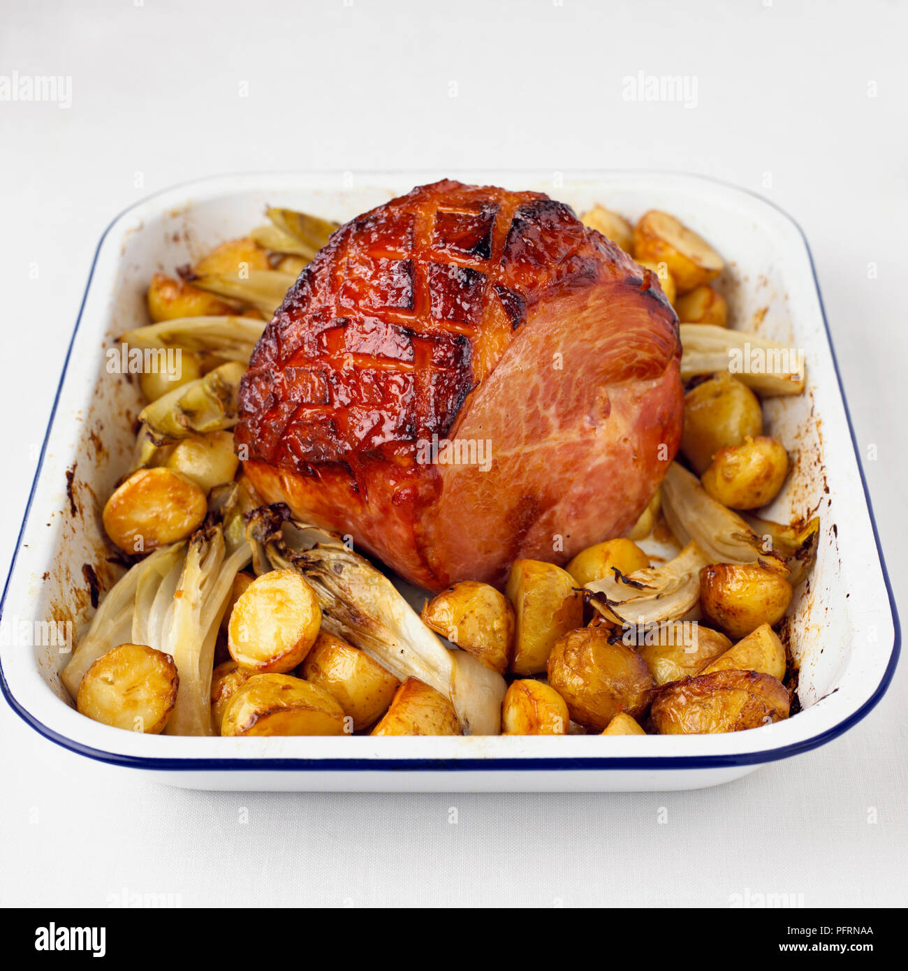 Marmalade-glazed gammon with new potatoes and chicory in tin roasting pan Stock Photo