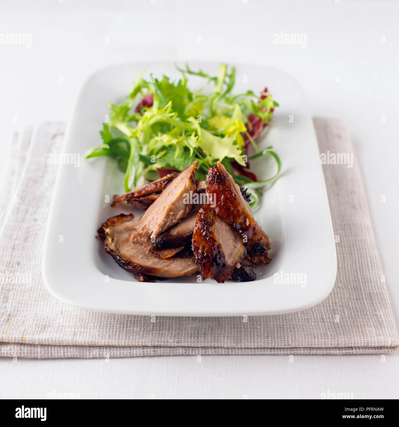 Crispy duck char sui served with lettuce in long white dish on folded tablecloth, close-up Stock Photo