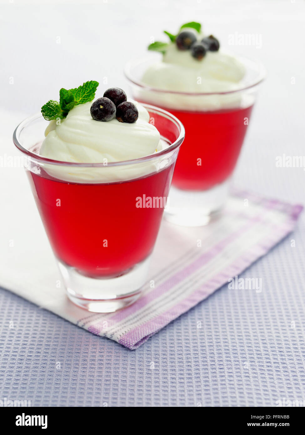 Blackcurrant jelly with whipped vanilla cream served in glasses on napkin, closeup Stock Photo