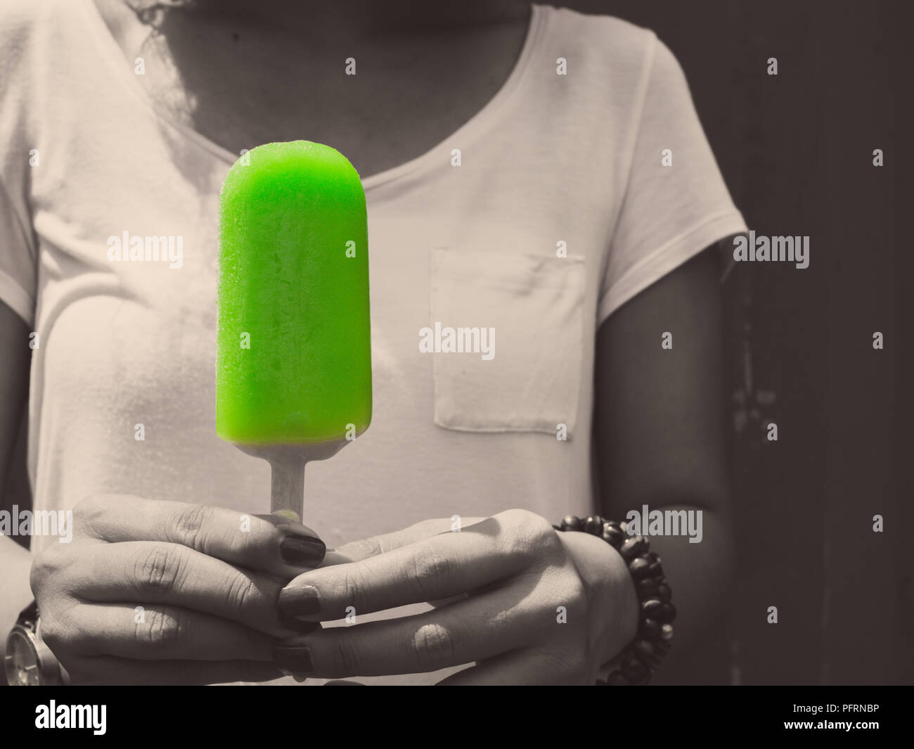 Woman Wearing White Shirt Holding Green Frozen Popsicle Ice Pop on Grunge Wall Background in Monochrome Art Style Stock Photo