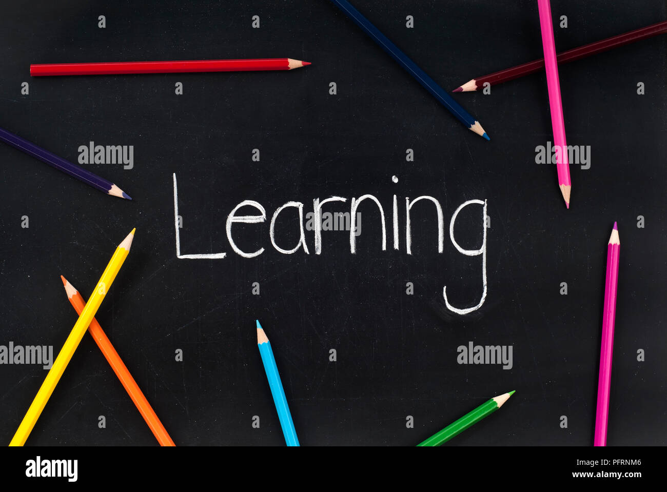 The word 'Learning' written in chalk on a blackboard, and some coloured pencils Stock Photo