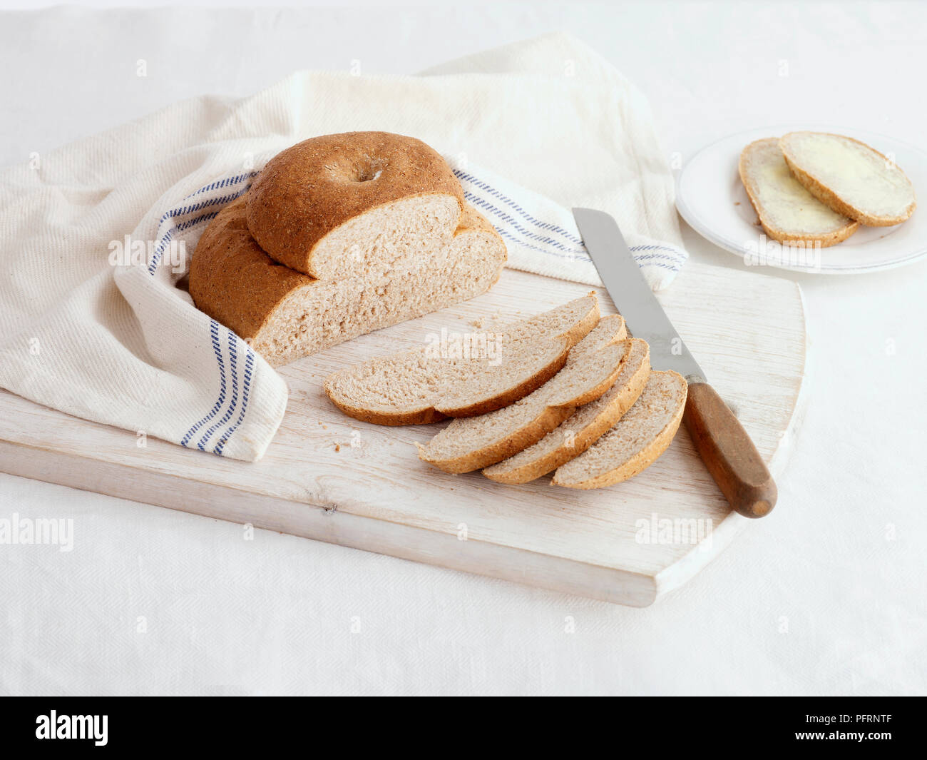 Sliced wholemeal cottage loaf with and without butter on chopping board ...